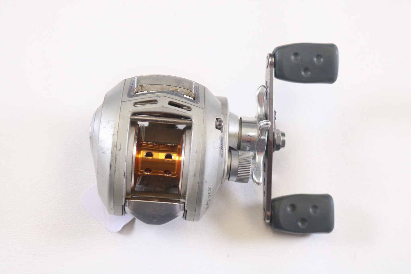 The Abu Garcia Revo STX Gen 1 7.1:1 RH, a used silver casting reel with a black handle and orange spool, shines against a white background, ideal for those in our Rod and Reel Trade-In Program seeking gear upgrades.